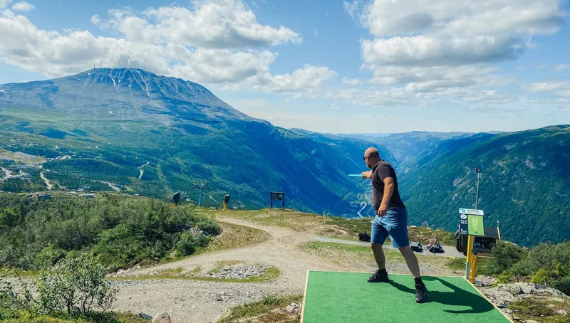 Frisbeegolfspiller på utslagsmatte på Gaustablikk med Gaustatoppen og Vestfjorddalen i bakgrunnen